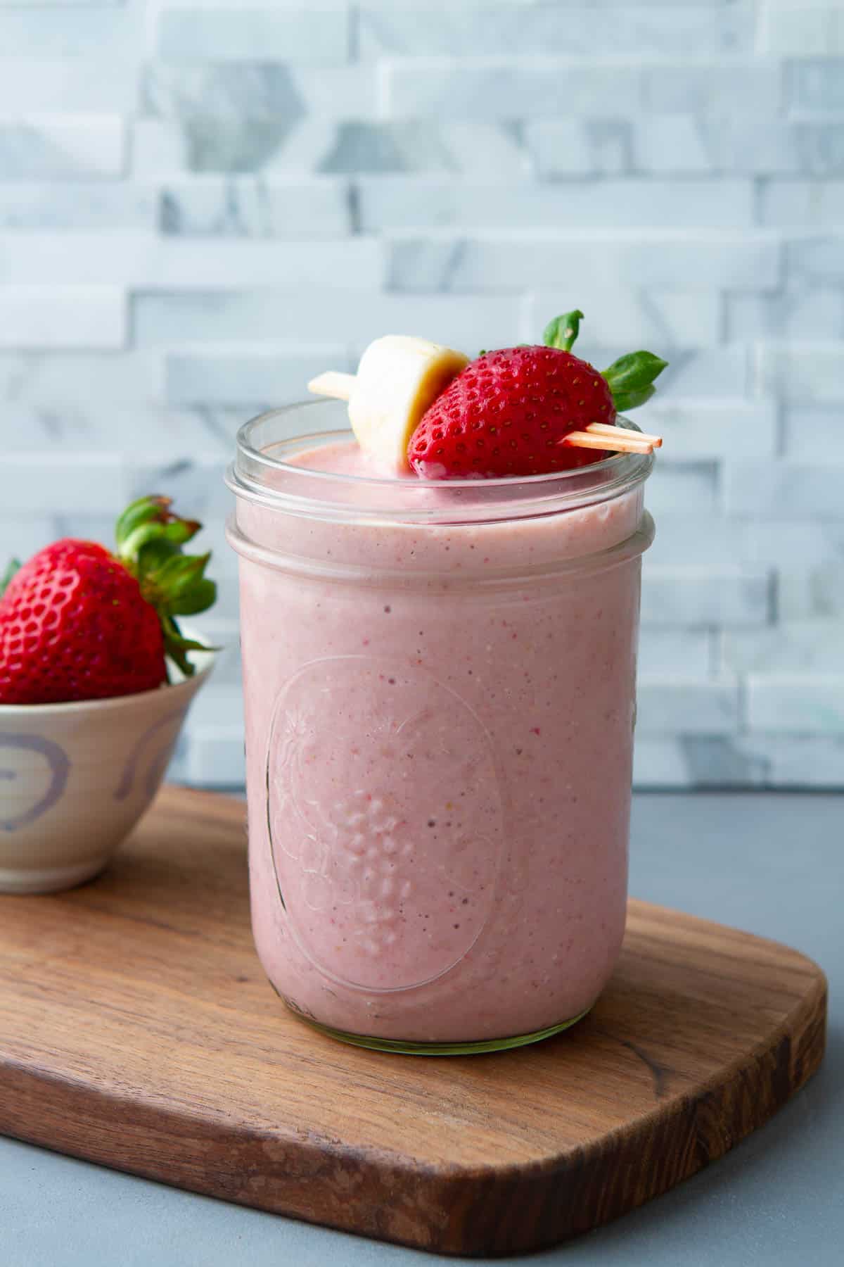 Mason jar filled with strawberry smoothie, on a wooden board.