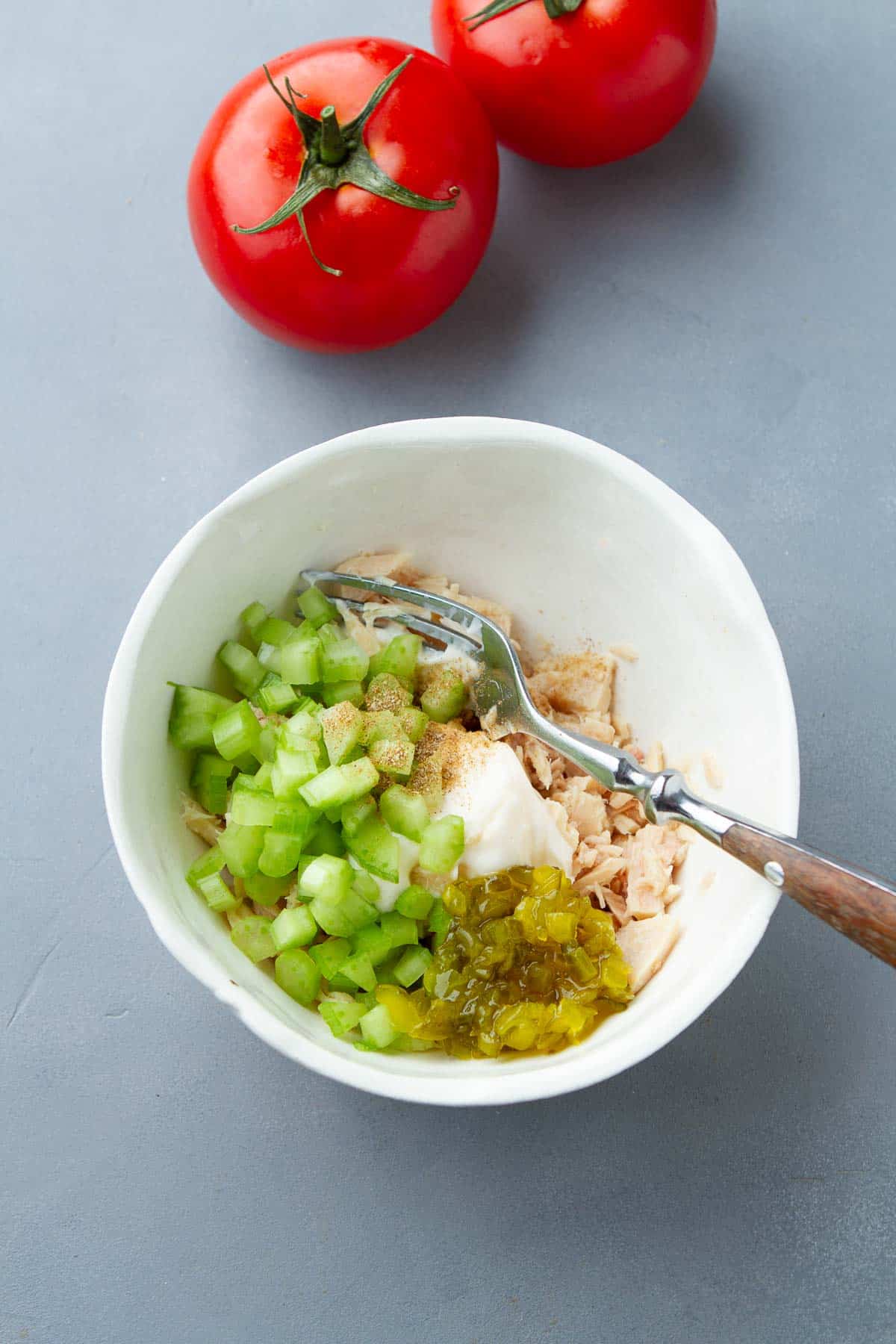 Tuna, mayonnaise, celery and relish in a white bowl.