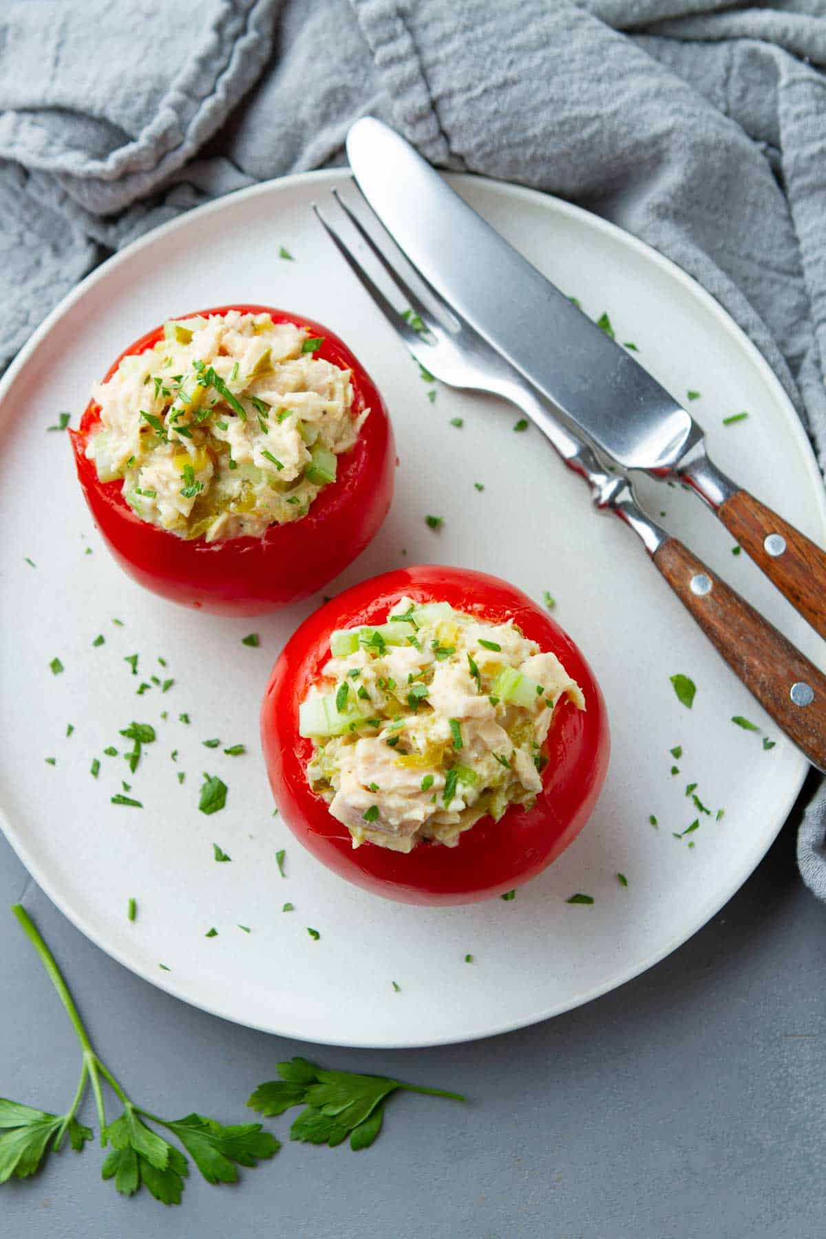 Tomatoes stuffed with tuna, knife and fork on a white plate.