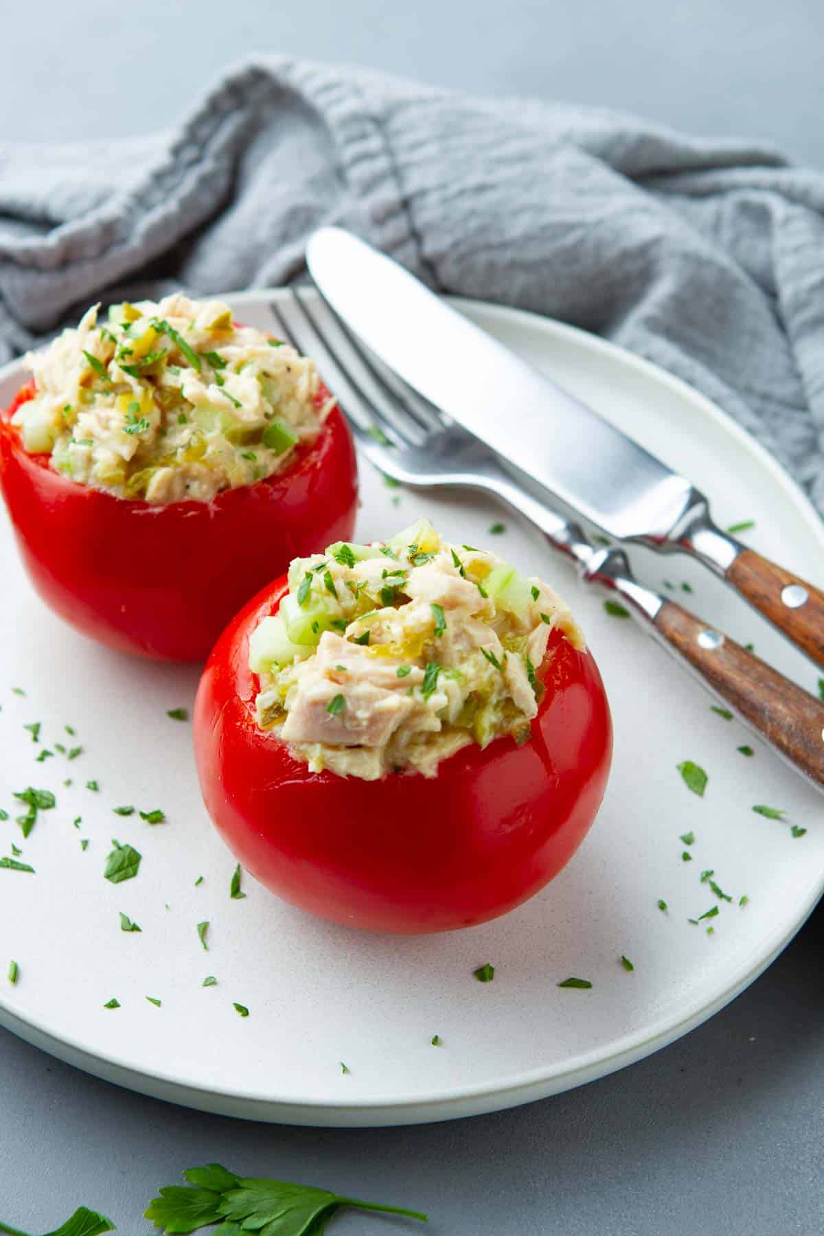 Tomatoes stuffed with tuna salad on a white plate with knife and fork.