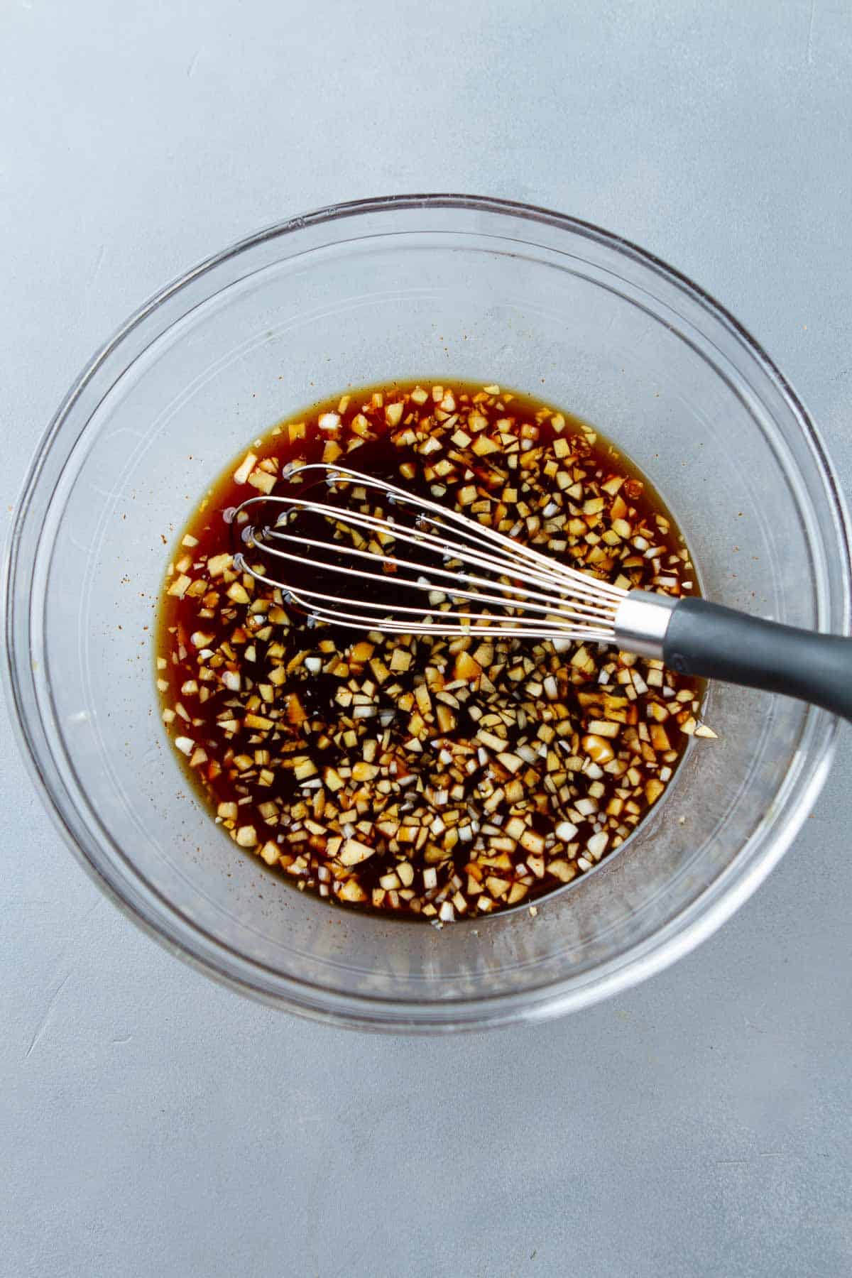Soy sauce, chopped ginger, garlic and a whisk in a glass bowl.