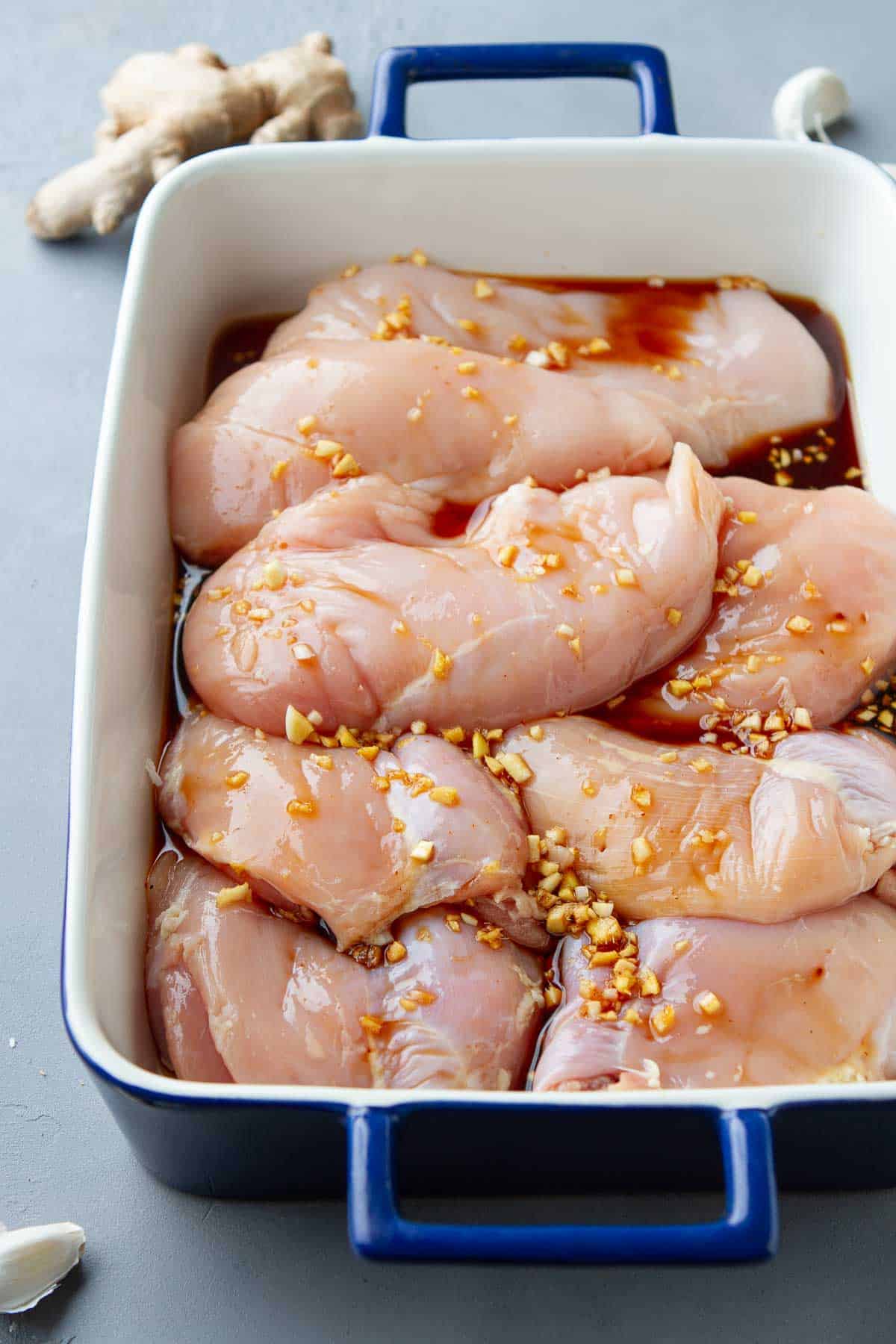 Chicken breasts marinating in a soy sauce marinade in a casserole dish.