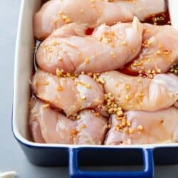 Raw chicken breasts, soy marinade and chopped garlic in a casserole dish.