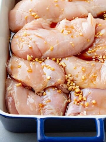 Raw chicken breasts, soy marinade and chopped garlic in a casserole dish.