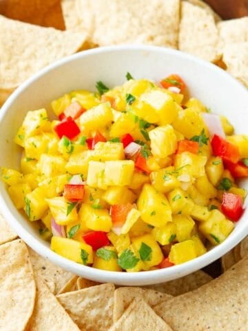 Pineapple and mango salsa in a white bowl, surrounded by tortilla chips.