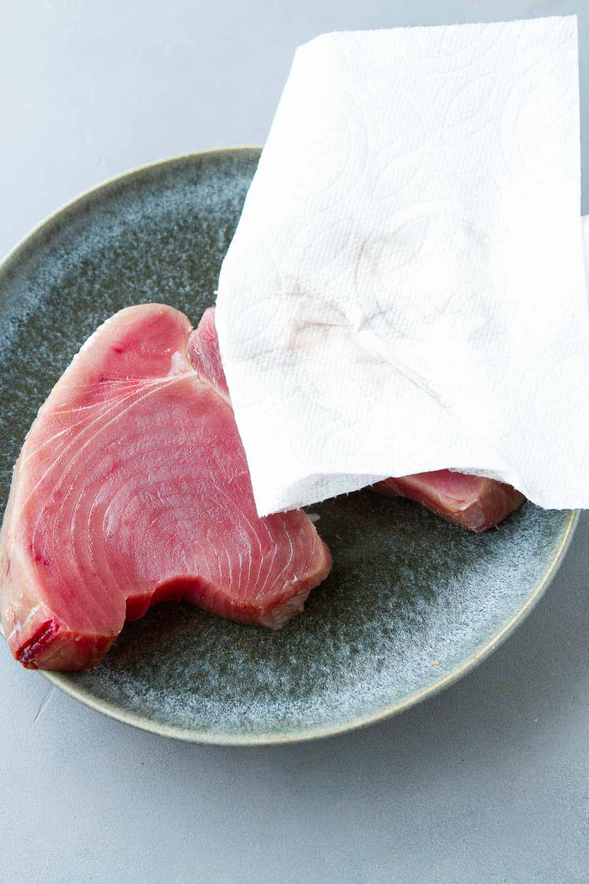 Raw tuna steaks on a plate with a paper towel on top.
