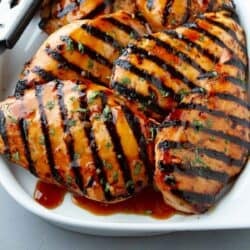 Grilled soy sauce chicken with sauce on a white plate.