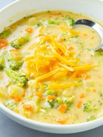 Broccoli cheese potato soup topped with grated Cheddar cheese in a white bowl.