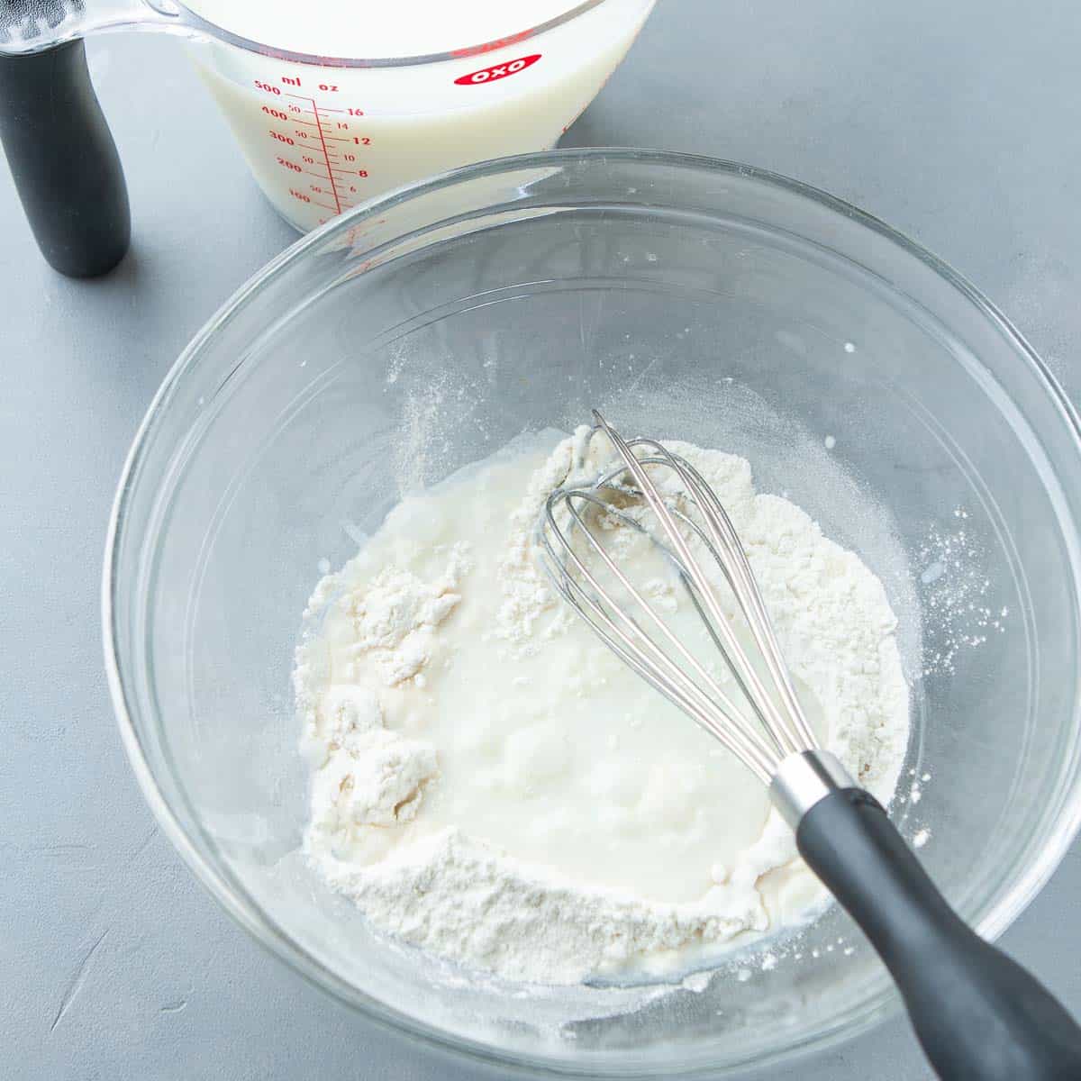Flour, milk and a whisk in a glass bowl.