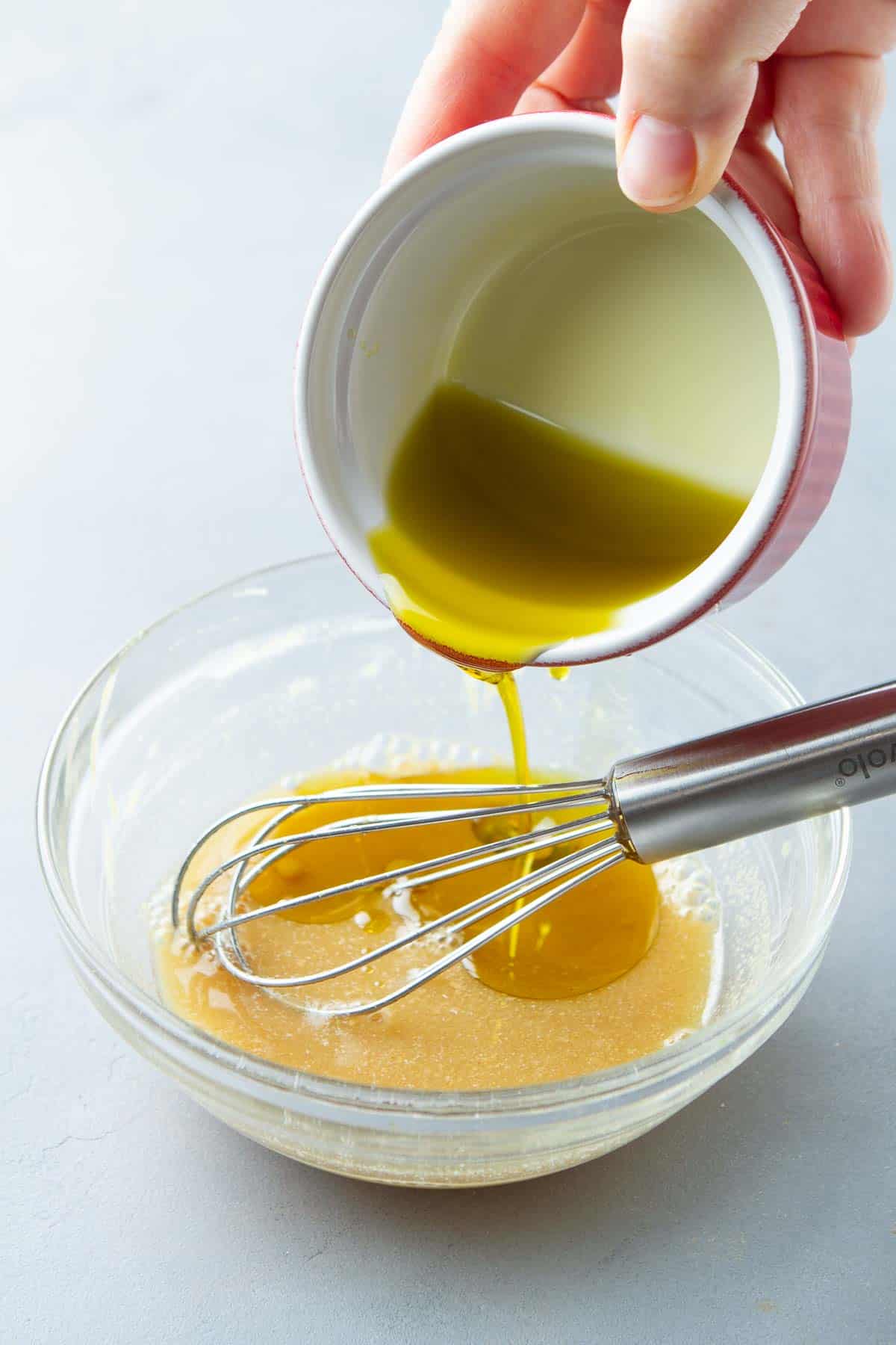Pouring olive oil into a glass bowl filled with salad dressing.