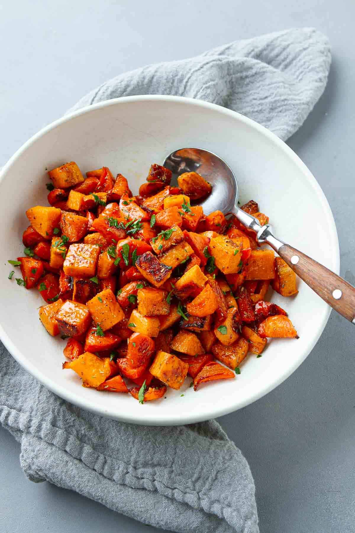 Chunks of cooked sweet potatoes and carrots in a white bowl with a spoon.