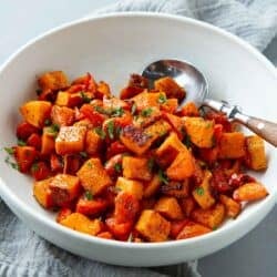 Roasted sweet potatoes and carrots, with a wooden-handled spoon, in a white bowl.