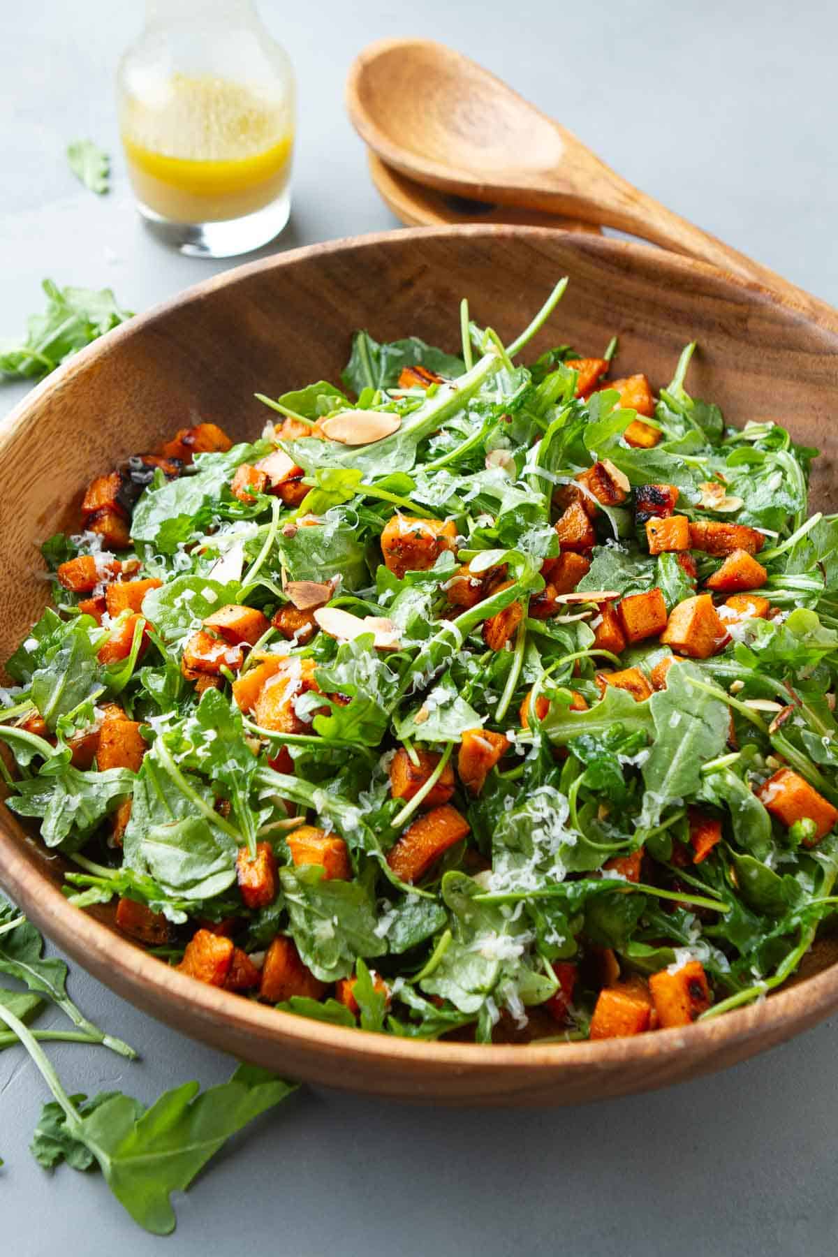 Arugula salad with sweet potato in a large wooden salad bowl.