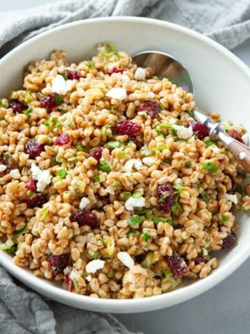 Farro salad with cranberries and goat cheese in a white bowl with a wooden-handled spoon.