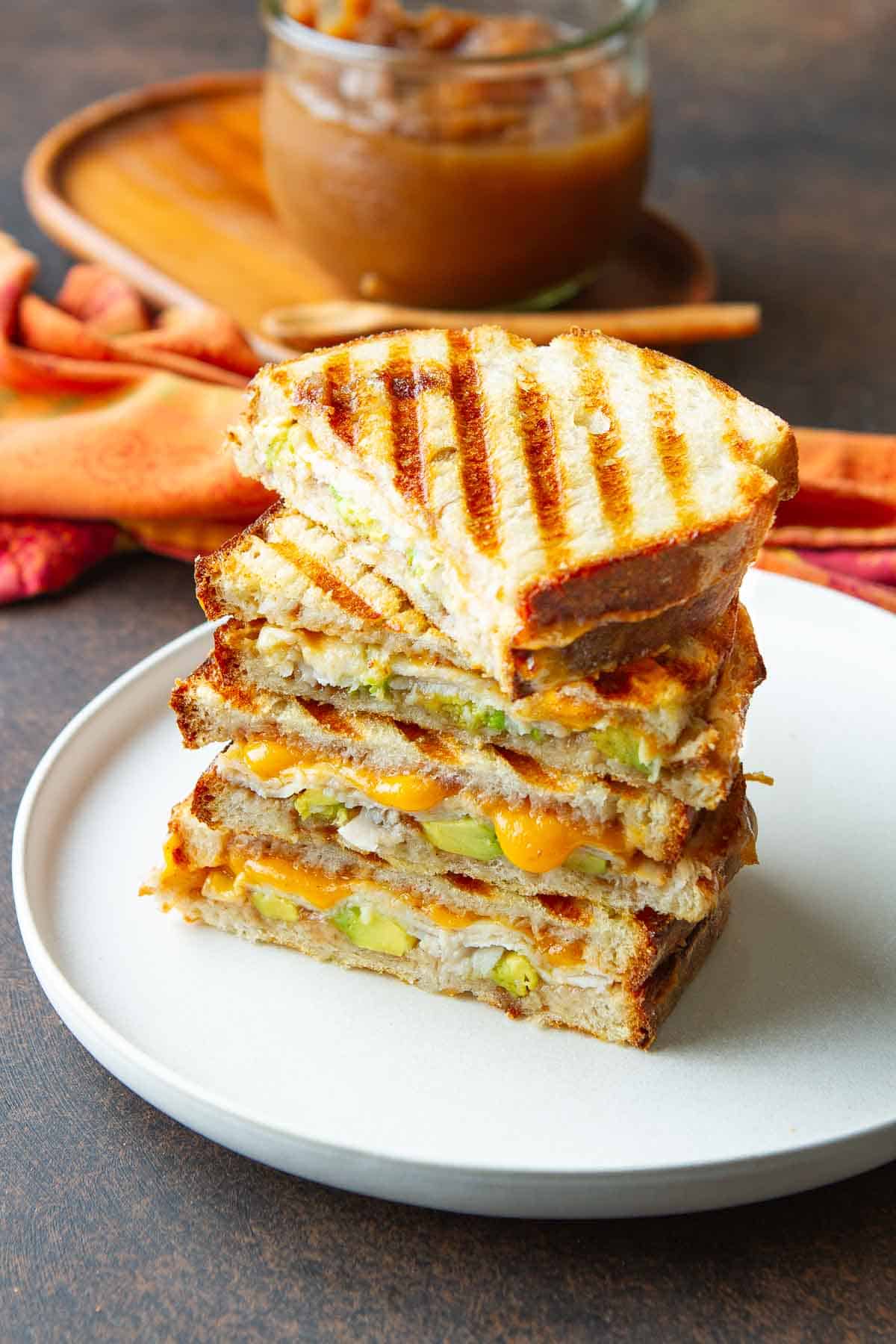 Two grilled cheese sandwiches with turkey and avocado on a white plate.