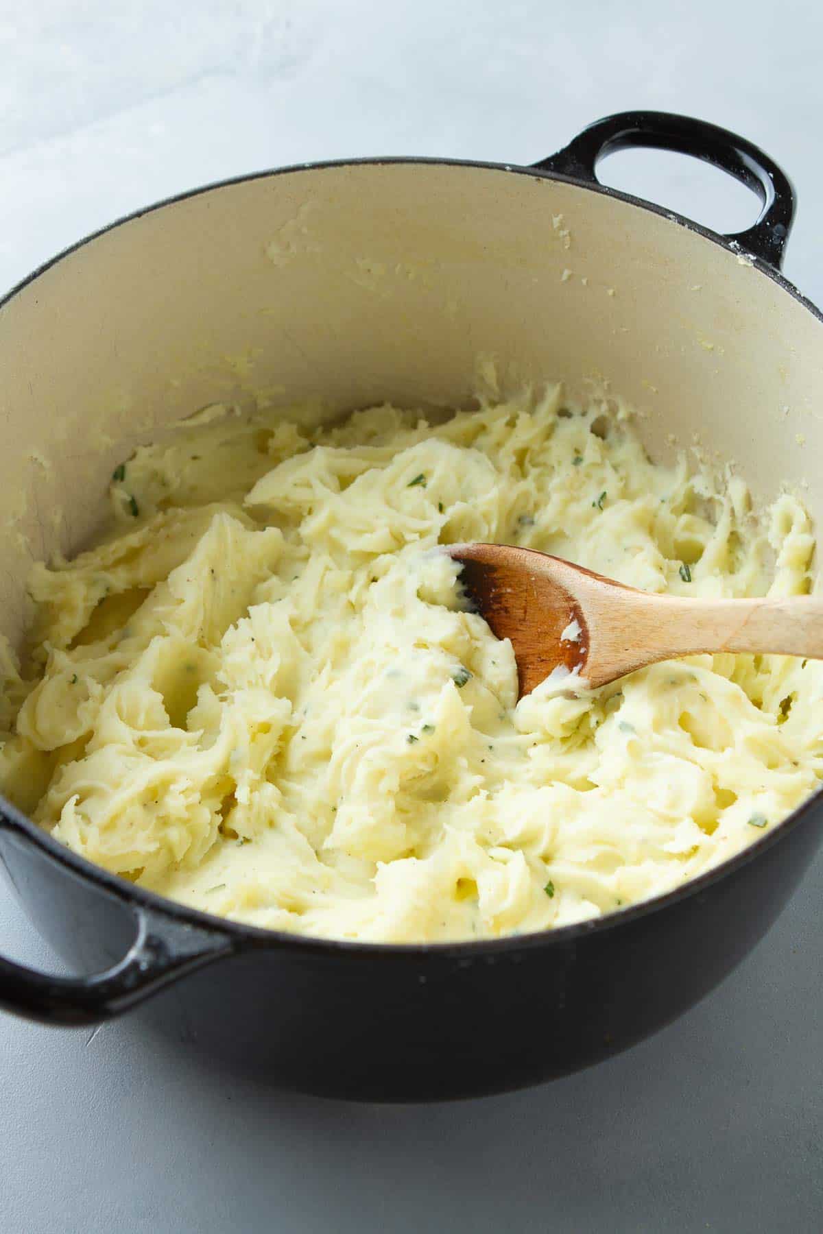 Mashed potatoes and a wooden spoon in a black Dutch oven.
