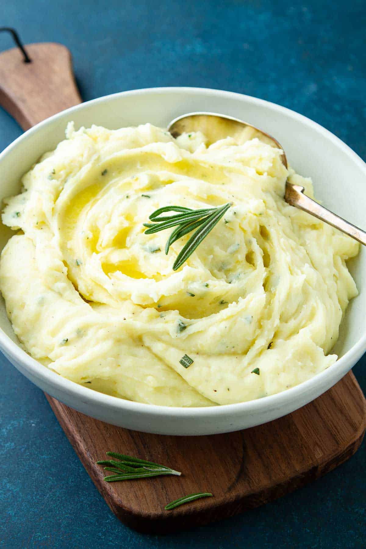 Rosemary mashed potatoes in a white bowl, resting on a small cutting board.