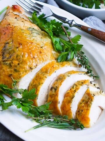 Partially sliced roasted turkey breast with parsley on a white plate.