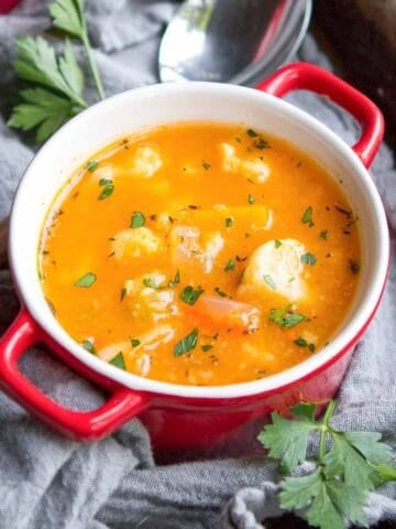Winter vegetable soup with cauliflower and squash in a small red and white bowl.