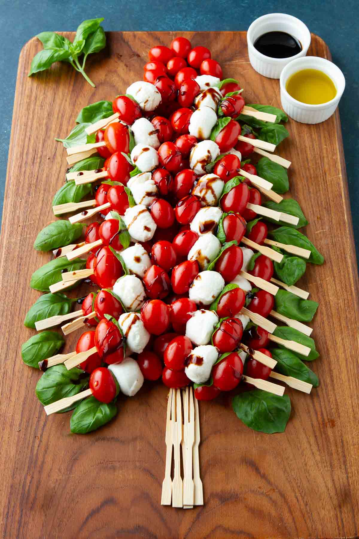 A Christmas tree formed out of tomato and mozzarella skewers on a wooden board.