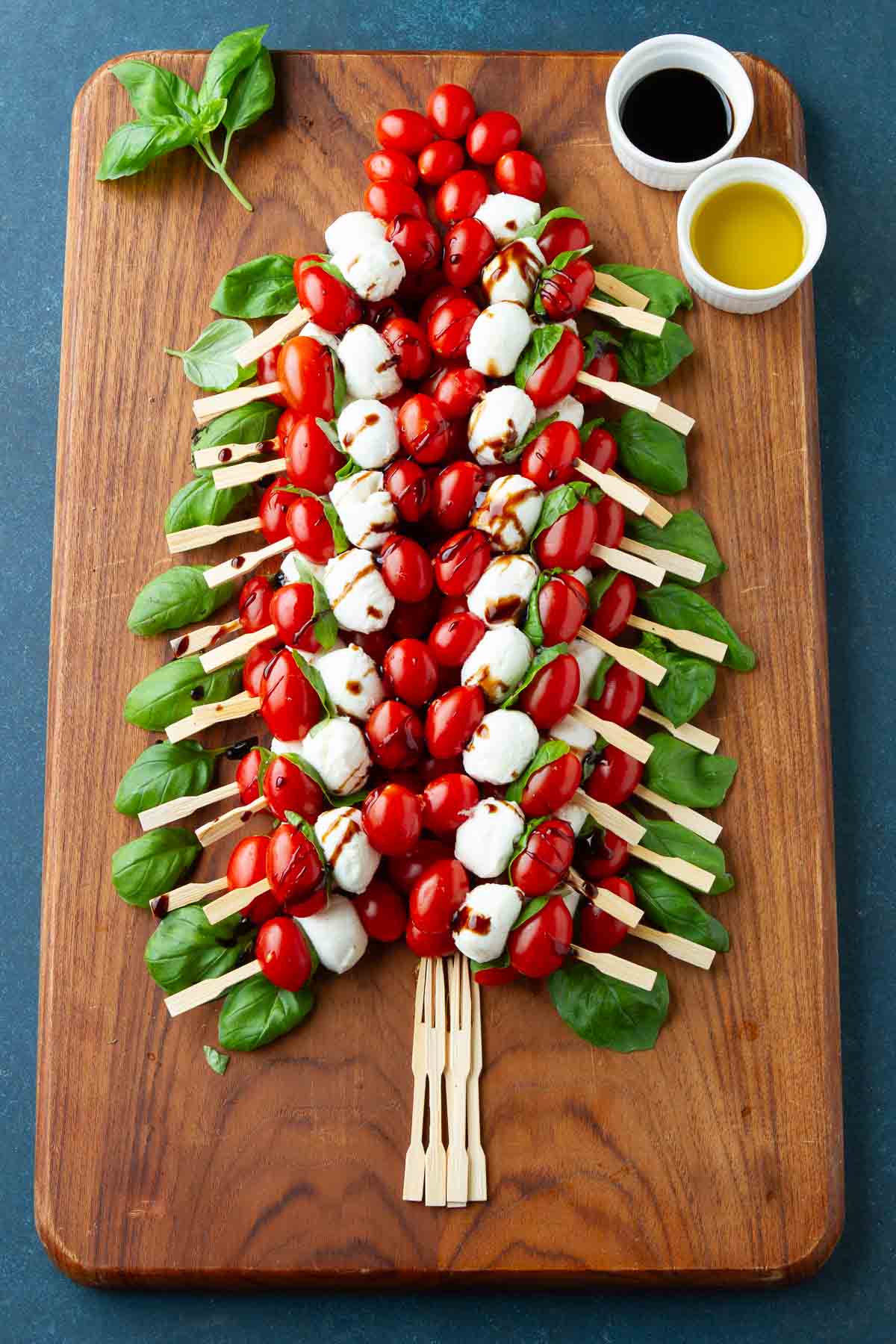 Caprese skewers arranged in the shape of a Christmas tree, on a wood board.