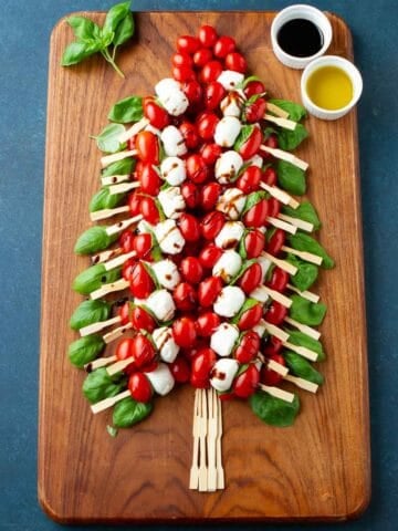 A Christmas tree made out of tomato, basil and mozzarella skewers on a wooden board.