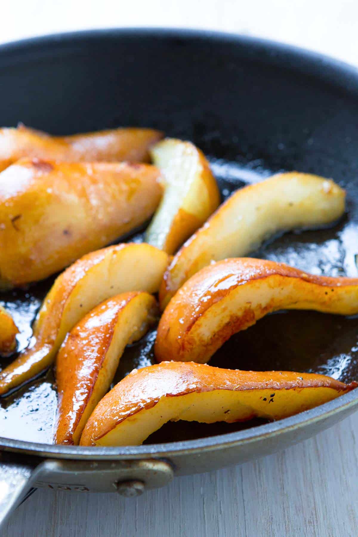 Golden brown pear slices, glazed with maple syrup, in a nonstick skillet.