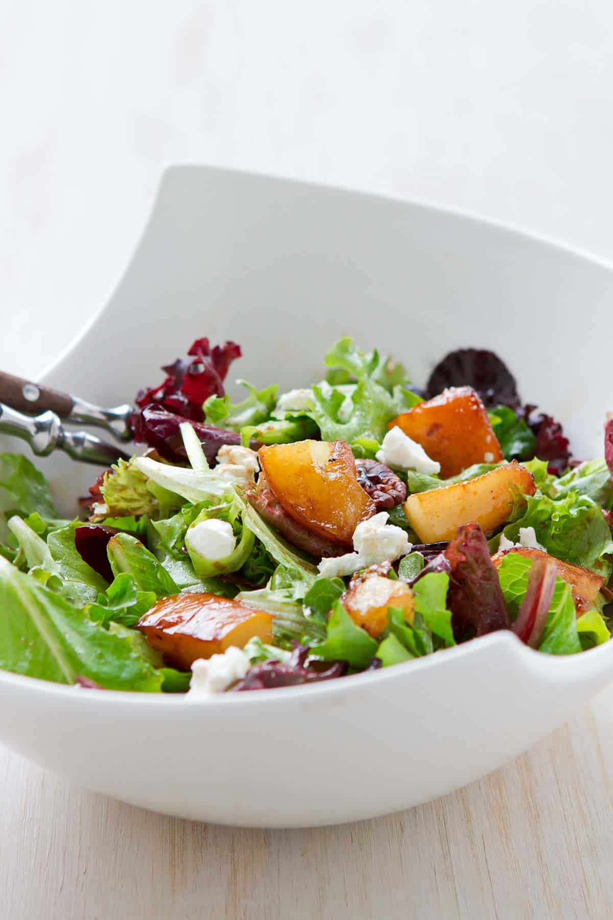 Pear salad in a large white bowl, with mixed greens, goat cheese and glazed pear chunks.