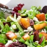 Glazed pears, greens, pecan and goat cheese in a white bowl.