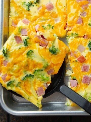 A sheet pan omelet with broccoli and ham, cut into squares.