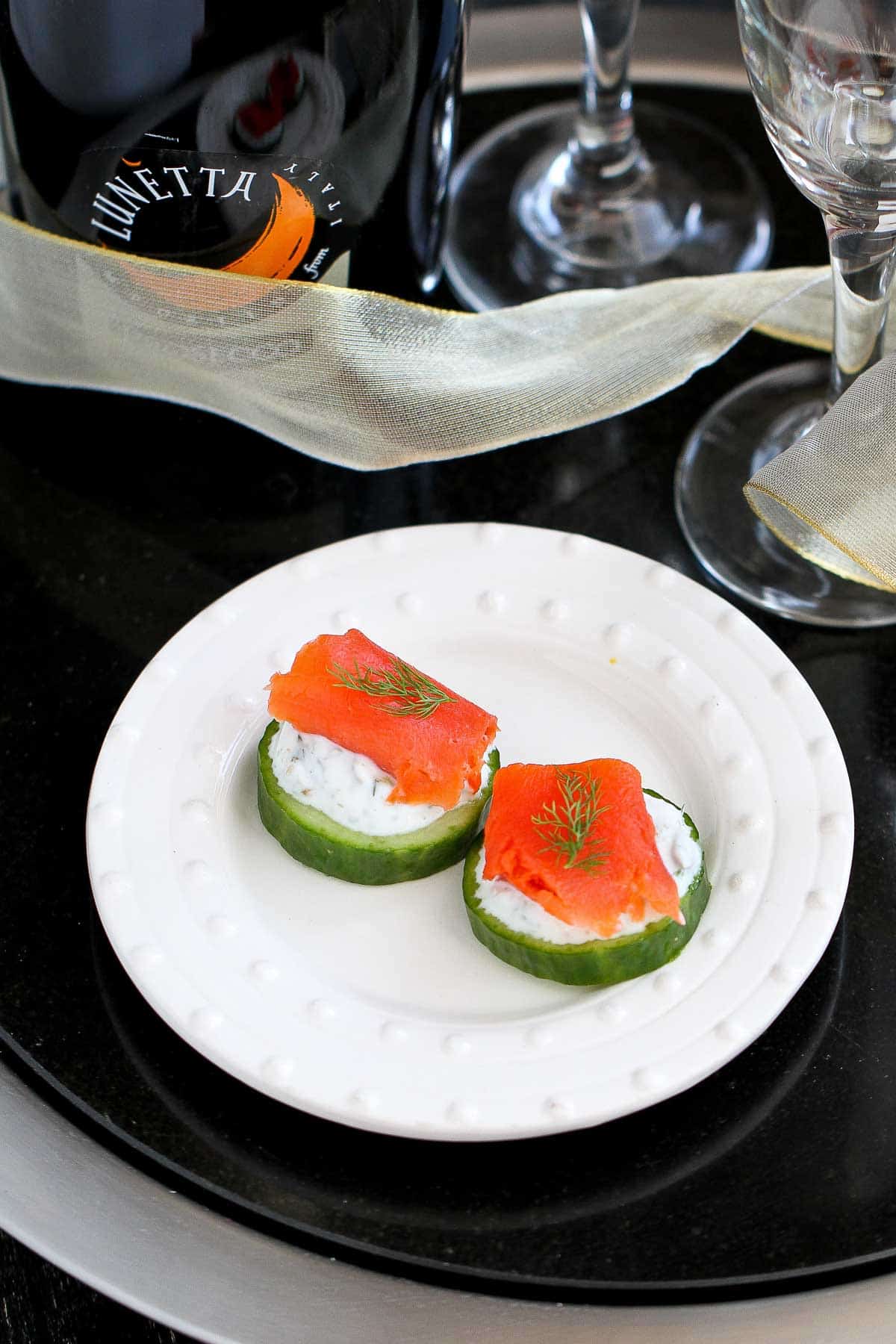 Two cucumber slices topped with yogurt and smoked salmon on a white plate.