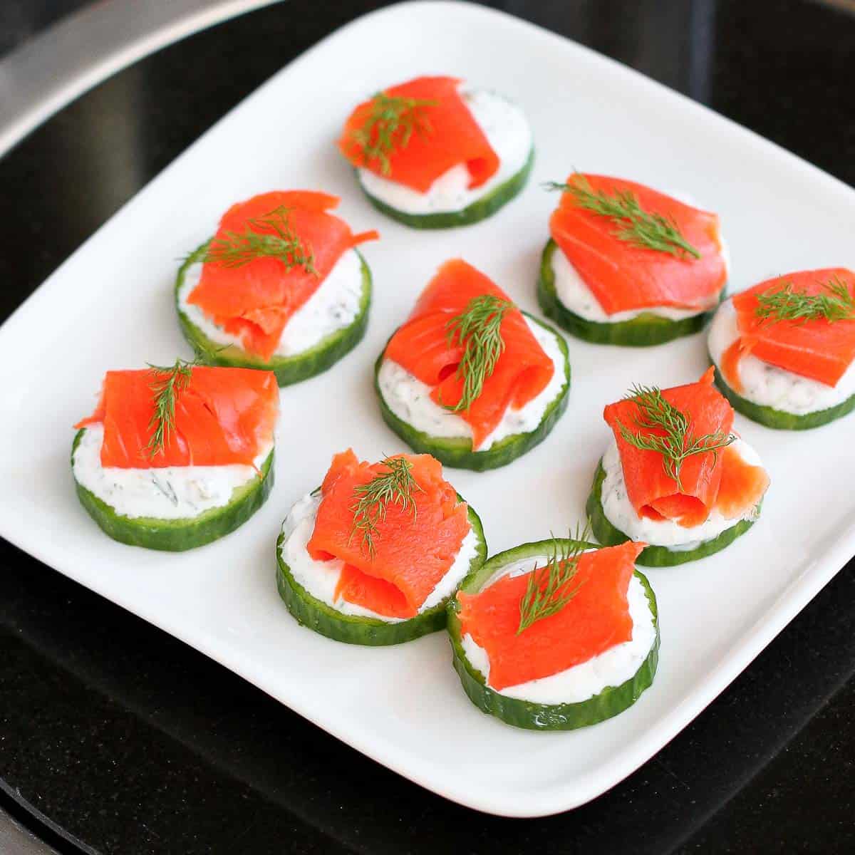 Smoked salmon and cucumber appetizers on a white plate.