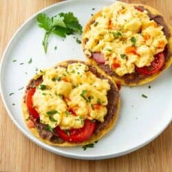 Two breakfast tostadas, topped with scrambled eggs, on a white plate.