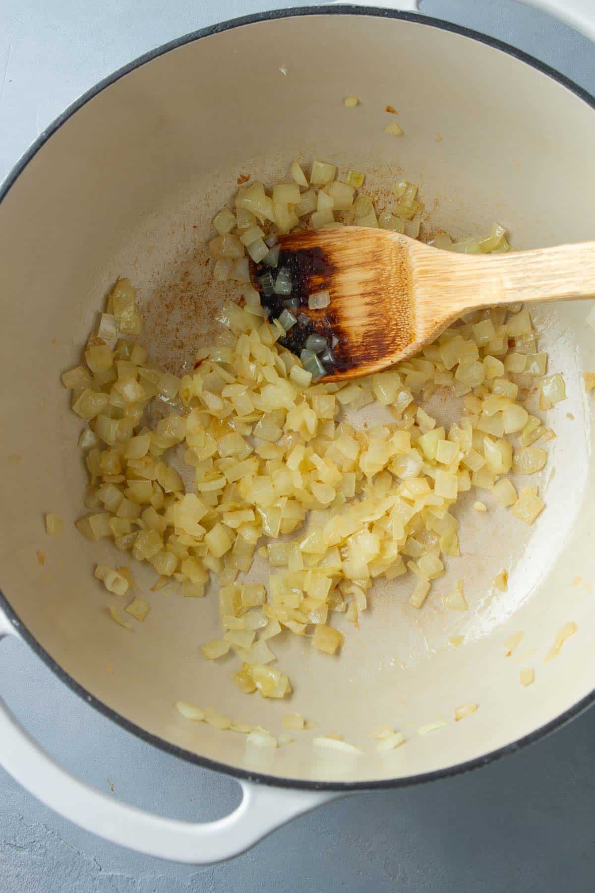 Cooked diced onions in a saucepan with a wooden spatula.