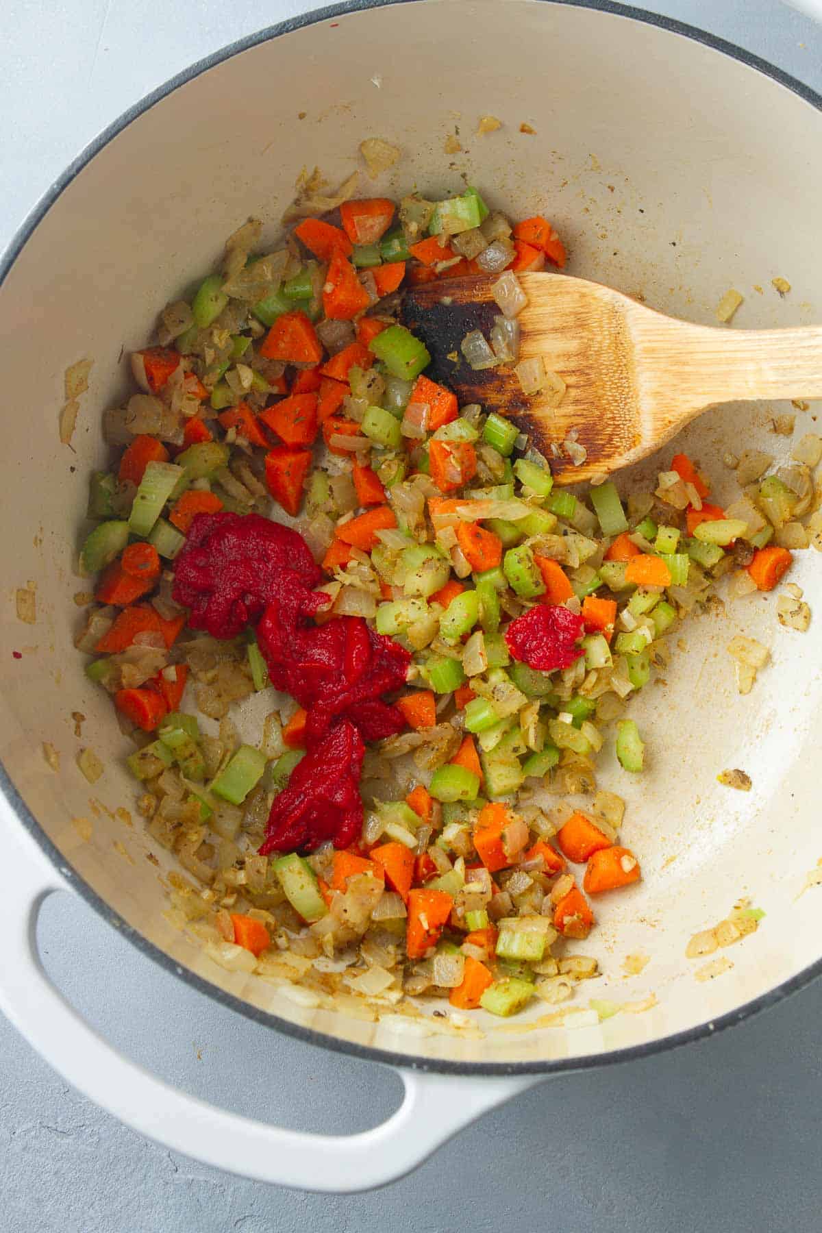 Tomato paste, carrots, onions and celery in a saucepan with a wooden spatula.