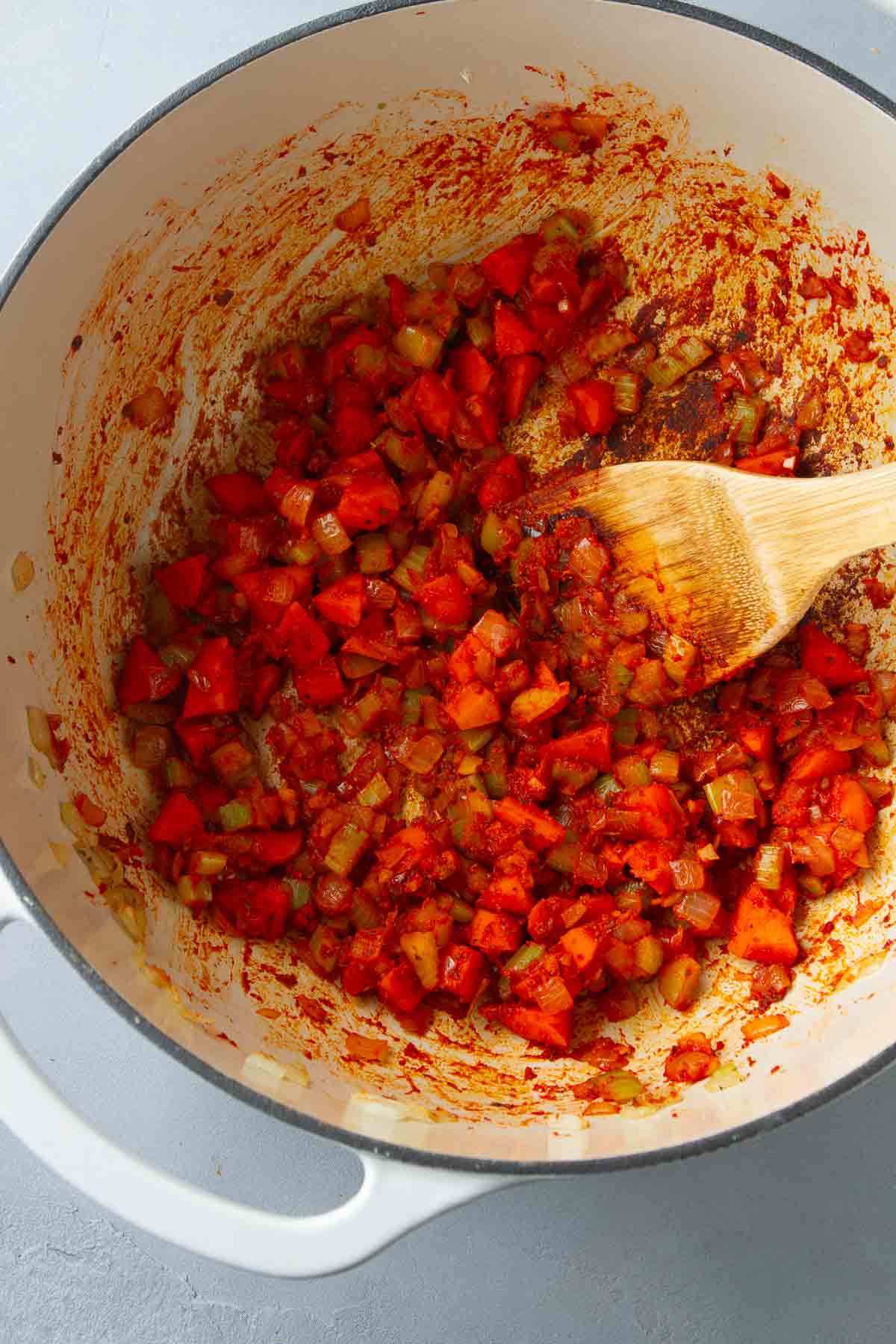 Chopped vegetables coated with tomato paste in a saucepan with a wooden spatula.