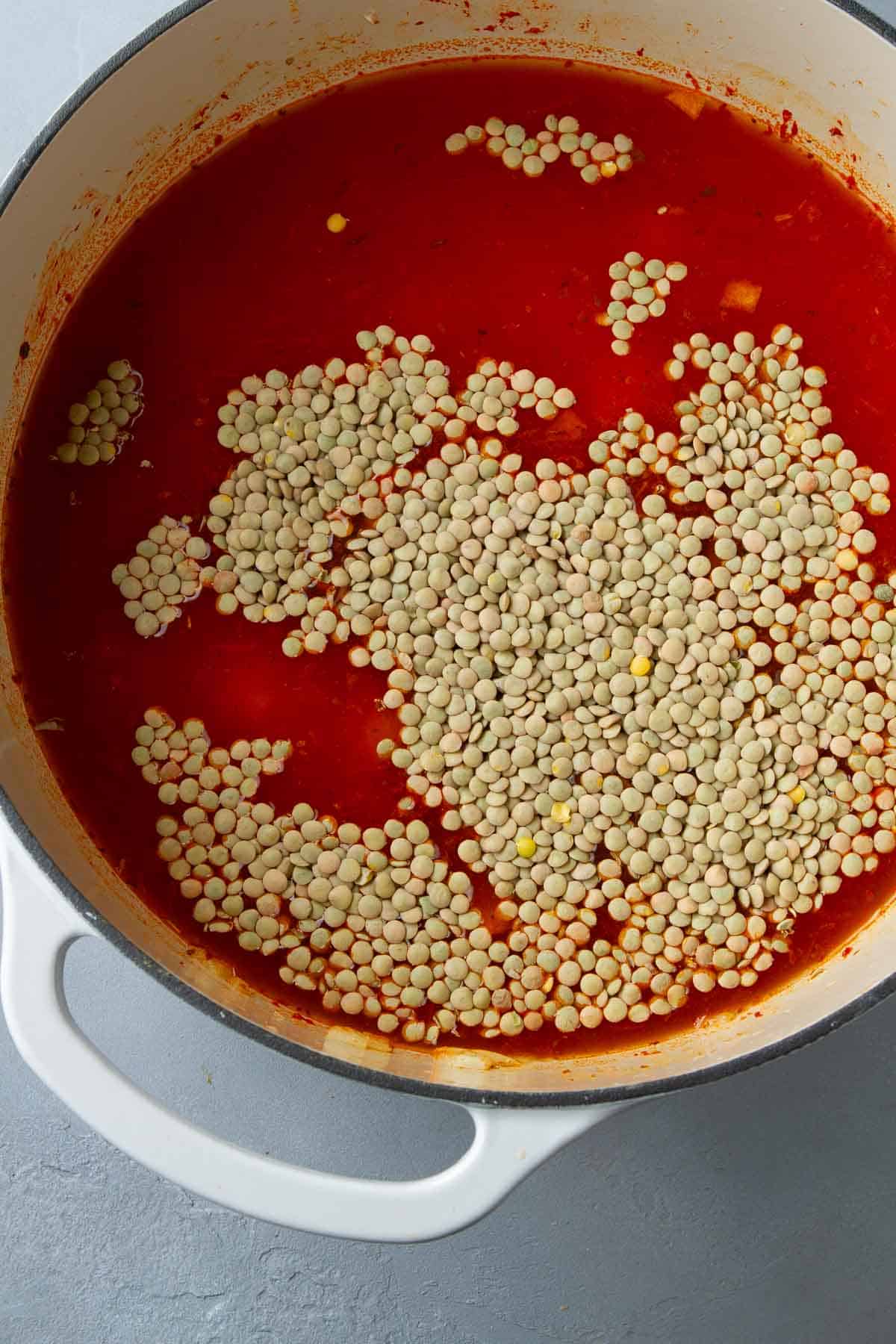 Uncooked lentils floating on the surface of vegetable broth in a large saucepan.