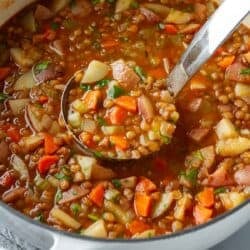 A ladleful of lentil and potato soup in a large saucepan.