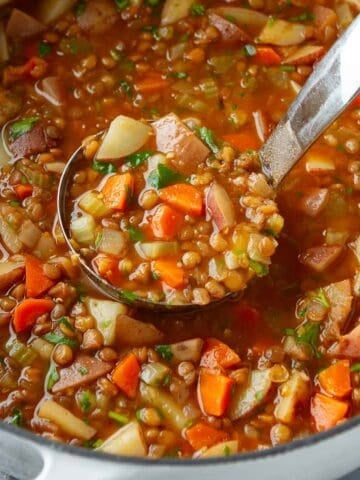 A ladleful of lentil and potato soup in a large saucepan.