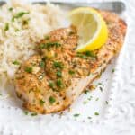Cooked pork chop, rice and lemon slice on a white plate.