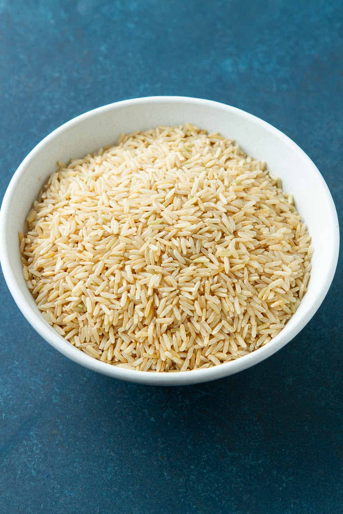 A white bowl filled with uncooked brown rice.