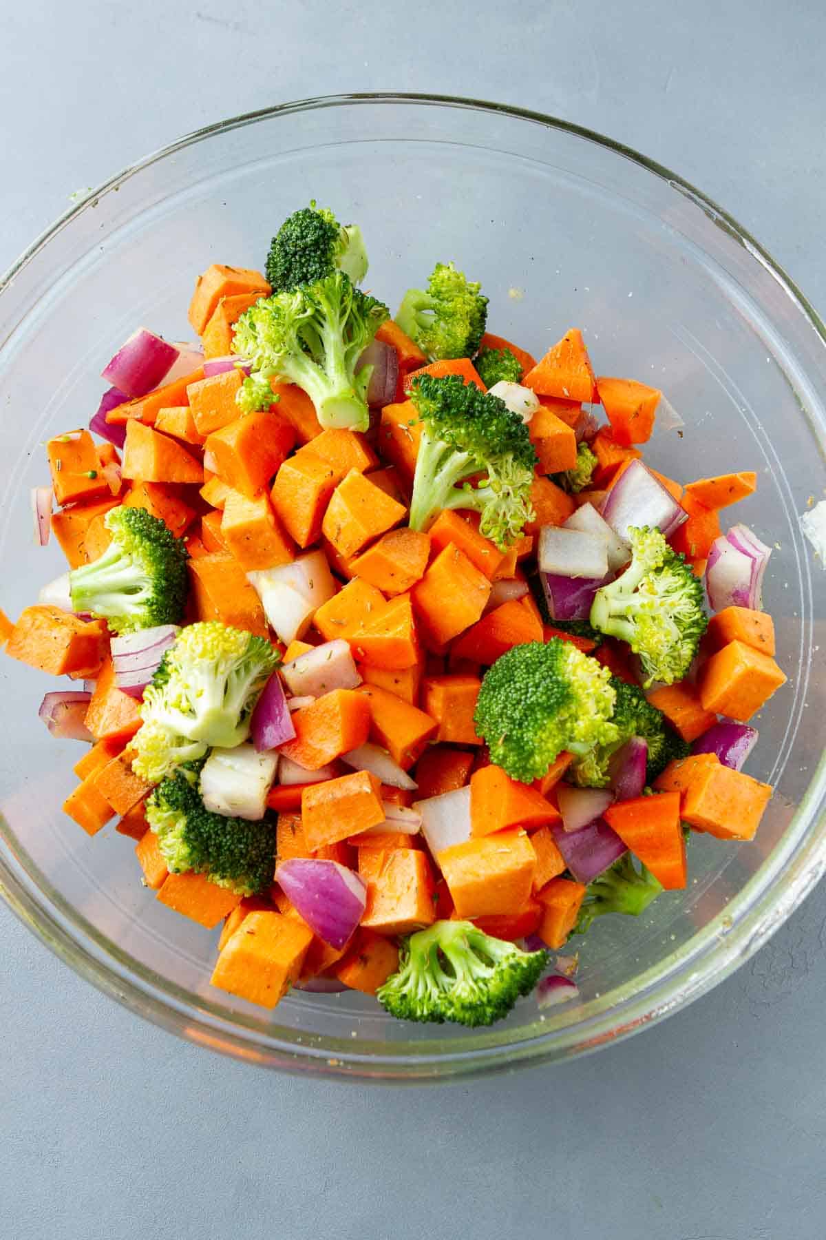 Chopped broccoli, sweet potato and red onion in a glass bowl.