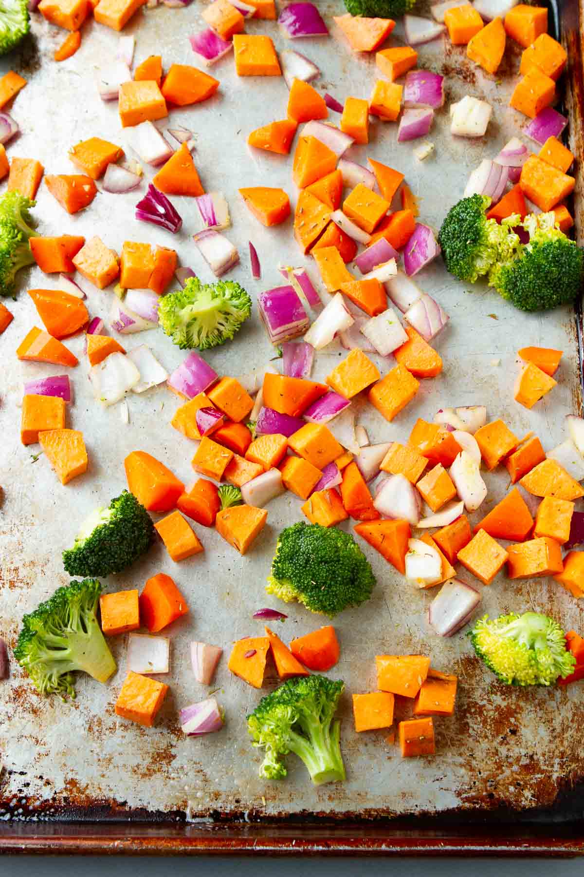 Chopped broccoli, sweet potato and red onion on a baking sheet.