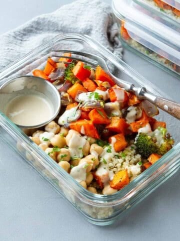 Roasted vegetables, chickpeas and quinoa drizzled with dressing in a meal prep container.