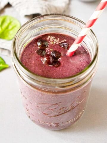Blueberry smoothie in a mason jar, with a red and white straw.