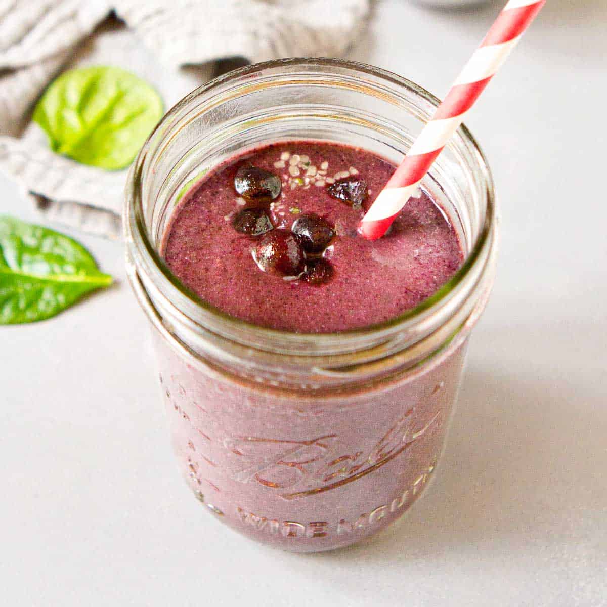 Blueberry smoothie in a mason jar, with a red and white straw.