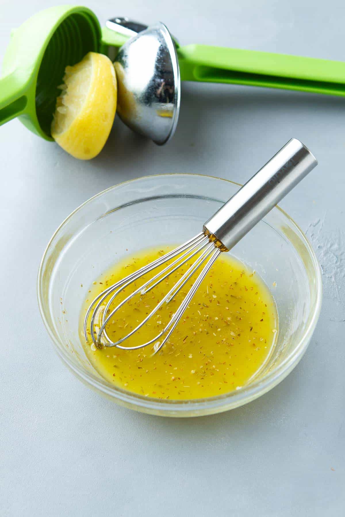Lemon juice, herbs and whisk in a bowl. Citrus juicer with a half lemon.