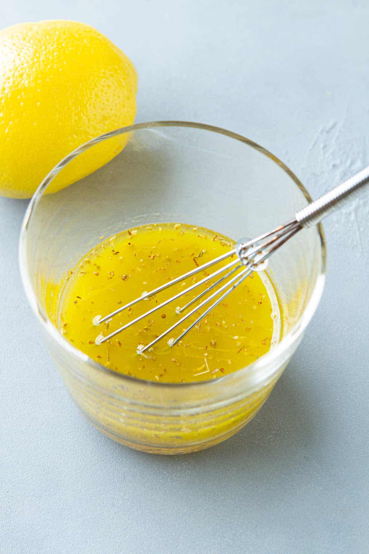 Lemon vinaigrette and a small whisk in a glass.