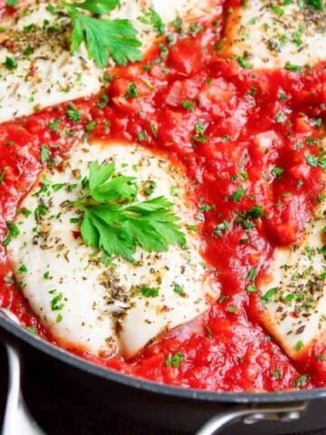 Cooked fish fillets with tomato sauce in a skillet.
