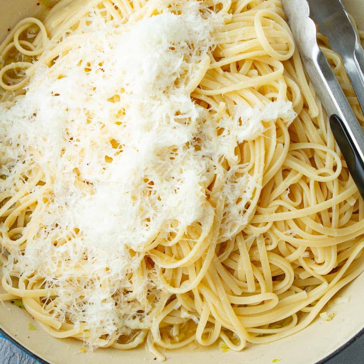 Pasta noodles and grated Parmesan cheese in a skillet.